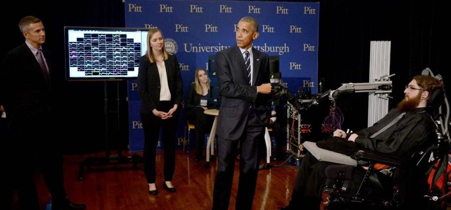 Scientists Rob Gaunt, Jen Collinger and Sharlene Flesher watch President Barack Obama bump fists with the robot arm that Nathan Copeland controls with his brain